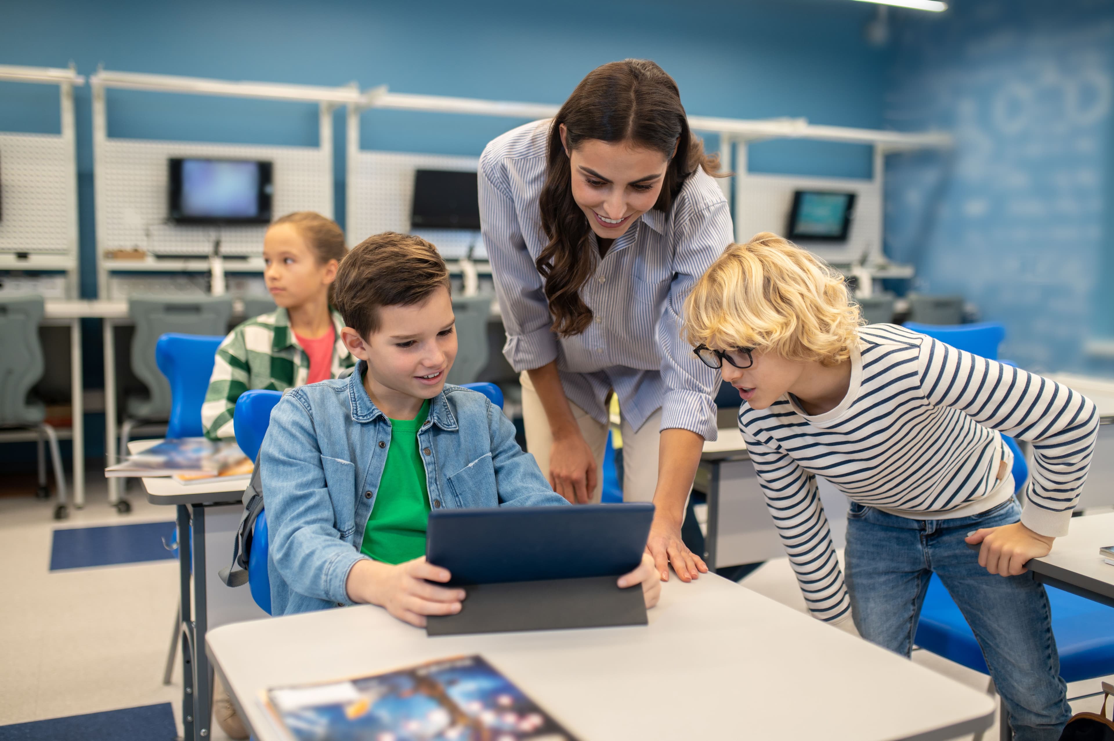 kvinde og to elever kigger på en bærbar computer i et klasseværelse
